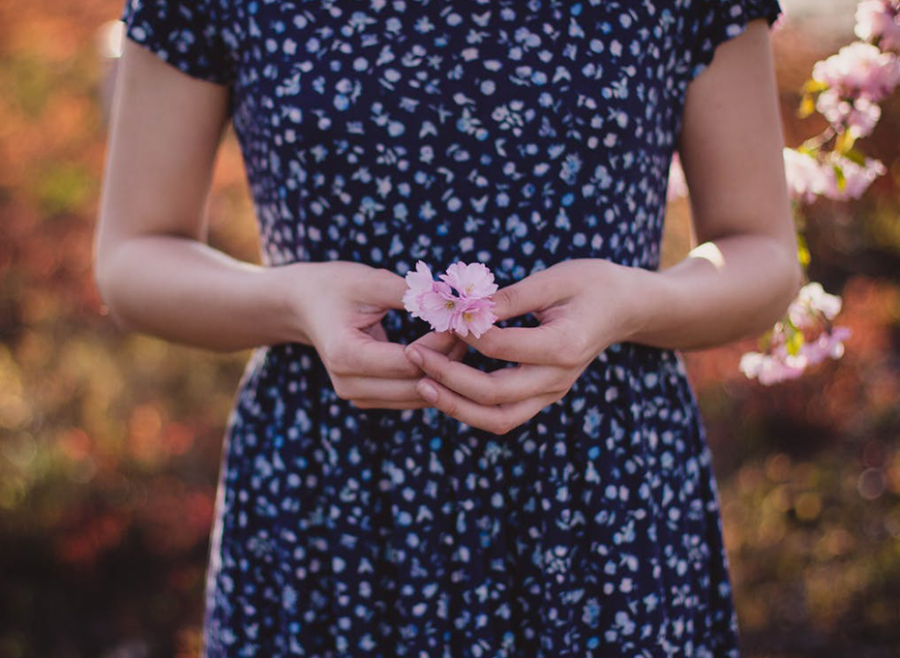różowe kwiaty w kobiecych dłoniach na tle kwiecistej sukienki